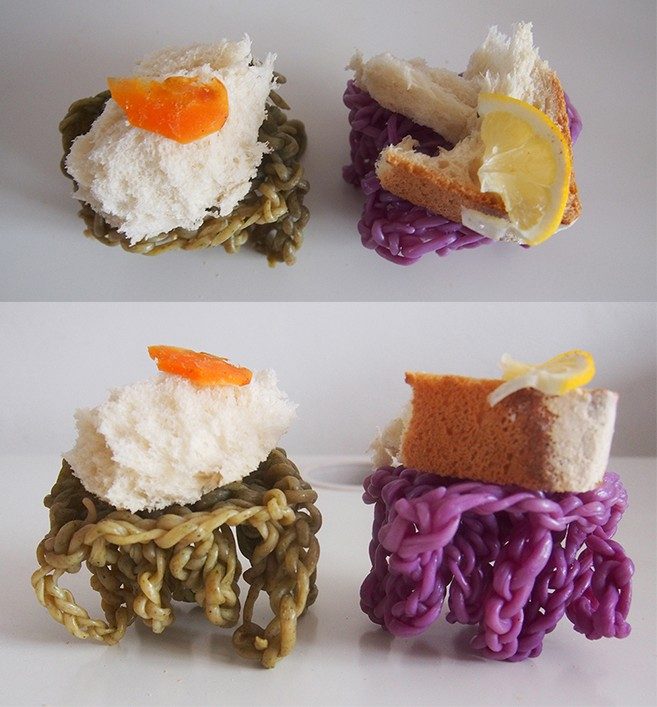 Green and purple knotted yarn forms topped with bread, orange peel and lemon