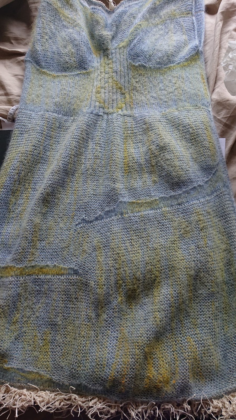 Blue-grey and yellow knitted dress laid flat with a fringed hem