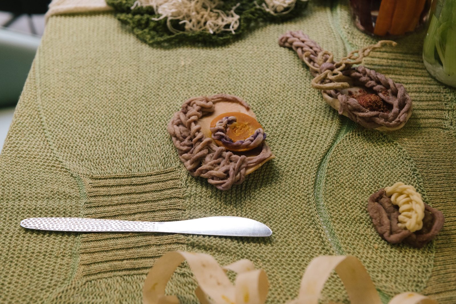 Knotted edible yarn pieces and a knife on a green knitted tablecloth