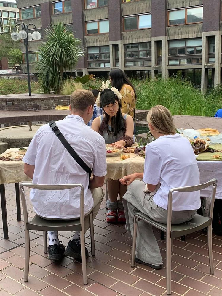 A woman wearing a knitted headpiece sitting at an outdoor table with two guests