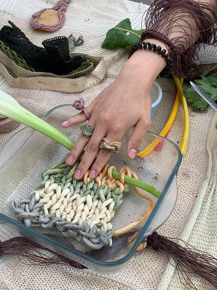 A hand pressing knotted edible yarn in a glass dish, with celery and a knitted bracelet