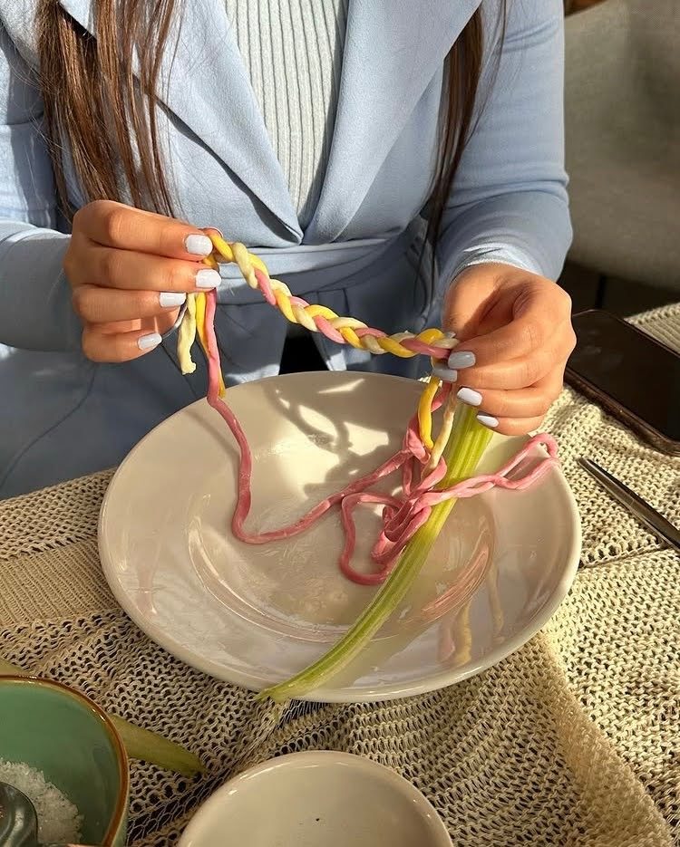 A woman pulling pink, yellow and white twisted edible yarn over a plate with a celery stalk