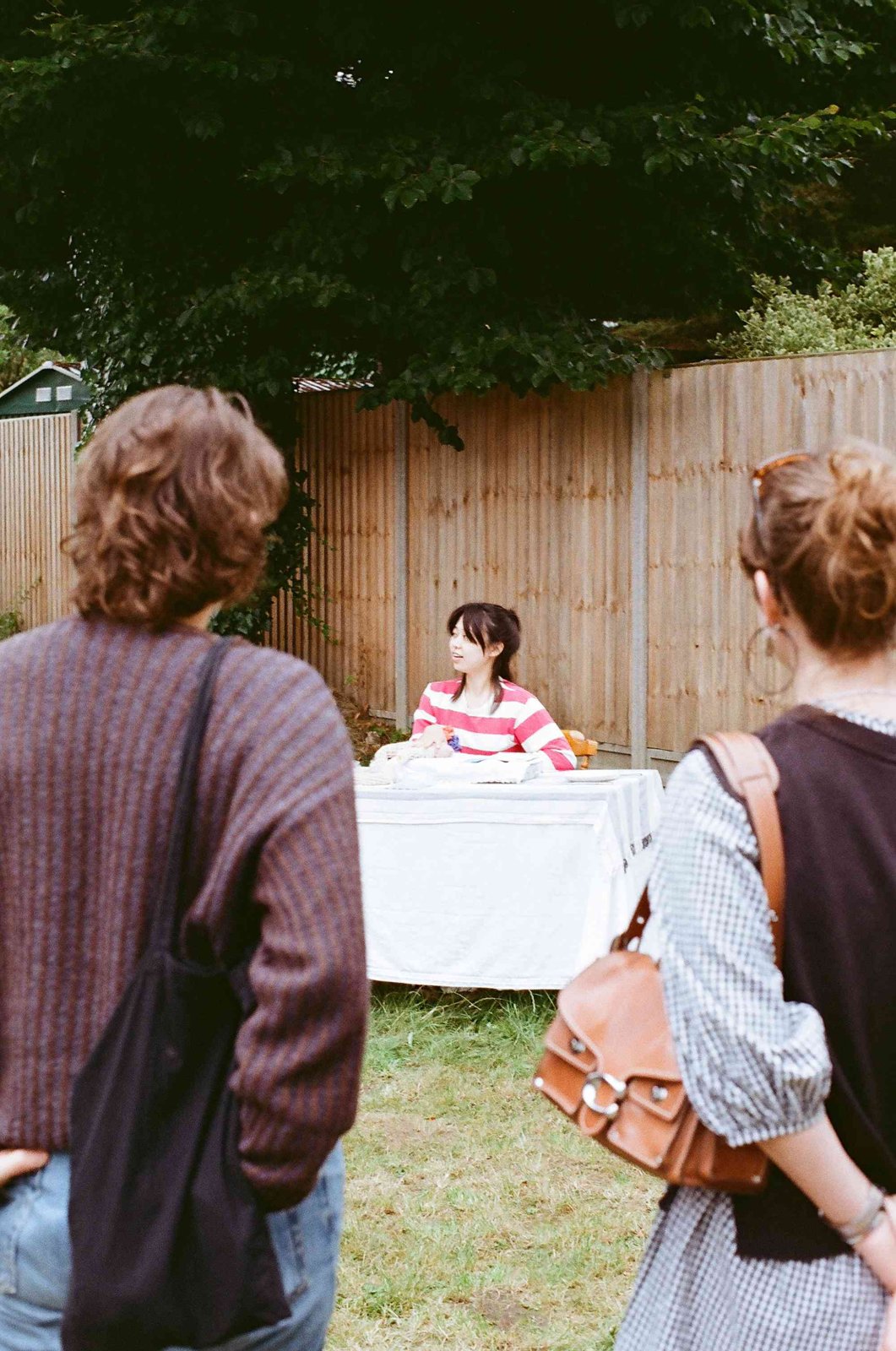 Two visitors watching the performer seated at a white-clothed table in a garden
