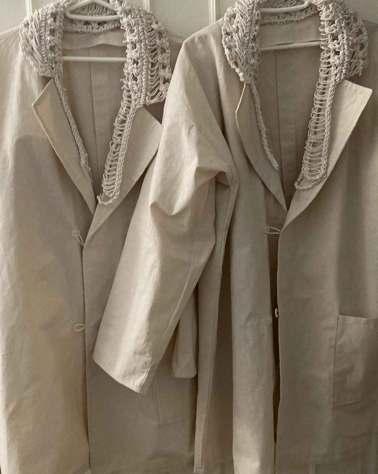 Two cream lab coats with knitted open-work collars on hangers