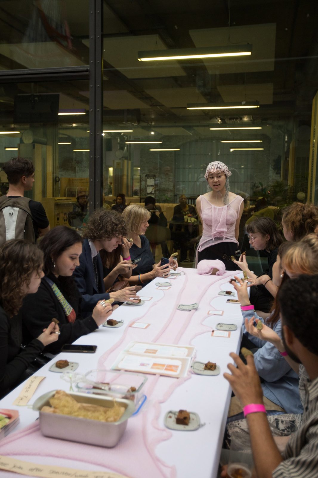 Participants eating around the long pink table during A Tin of Leftovers