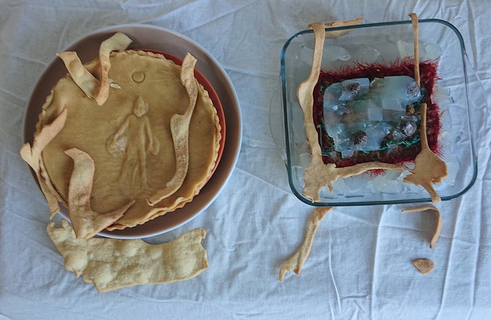 Top view of a treacle tart with a pressed figure and a glass dish of textile and ice on a white cloth