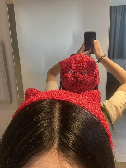 A woman wearing the red crocheted cat hat, taking a mirror selfie