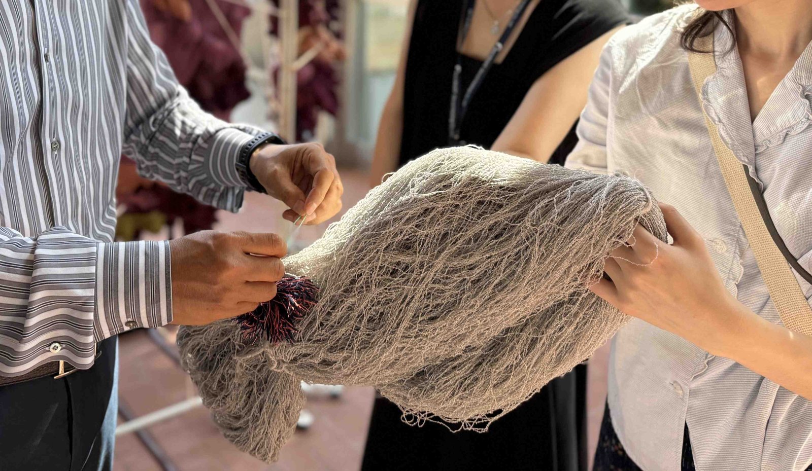 Hands pulling apart a grey knitted textile with purple tufts