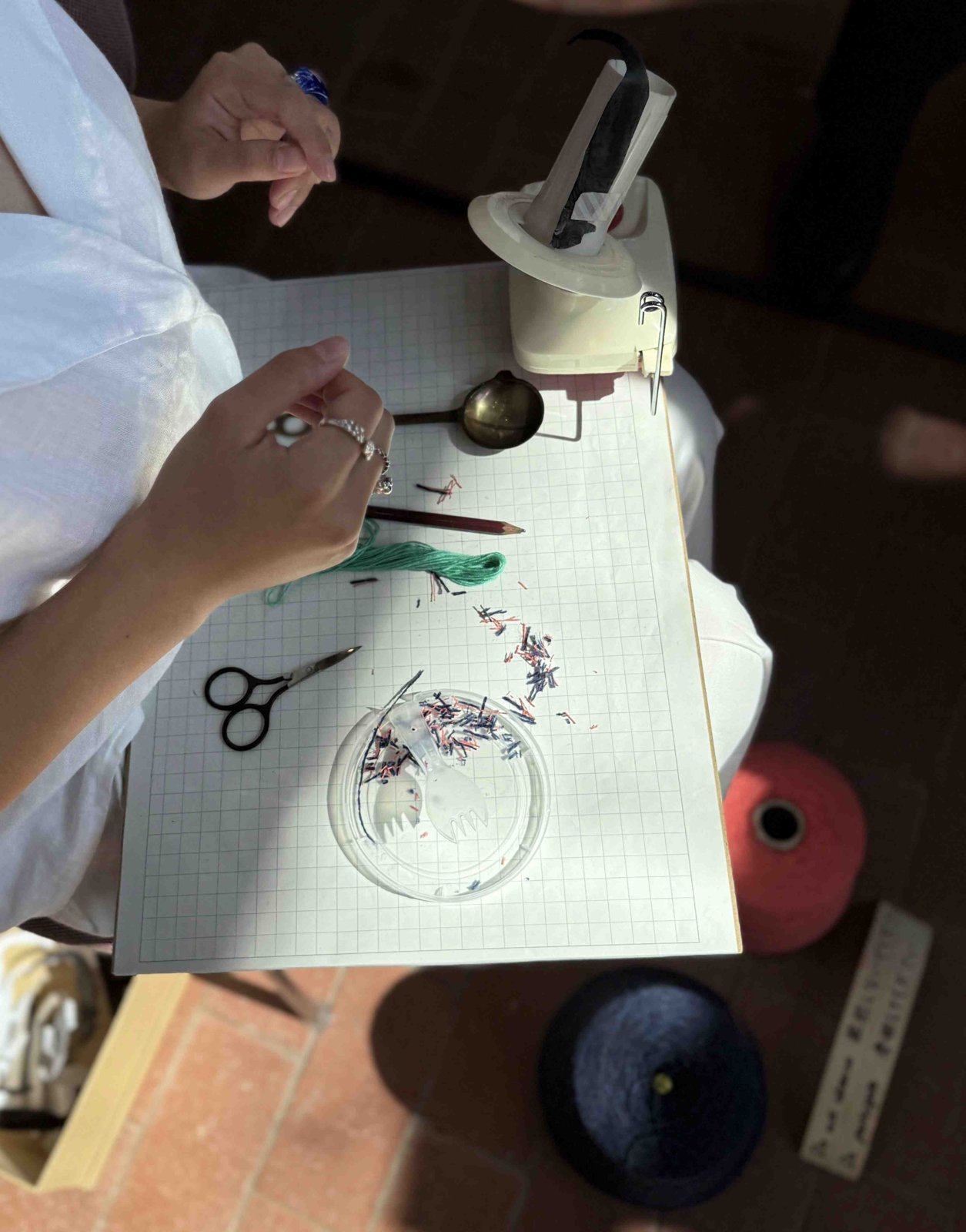 Top view of hands working at a table with a yarn winder, scissors and a glass dish of purple threads