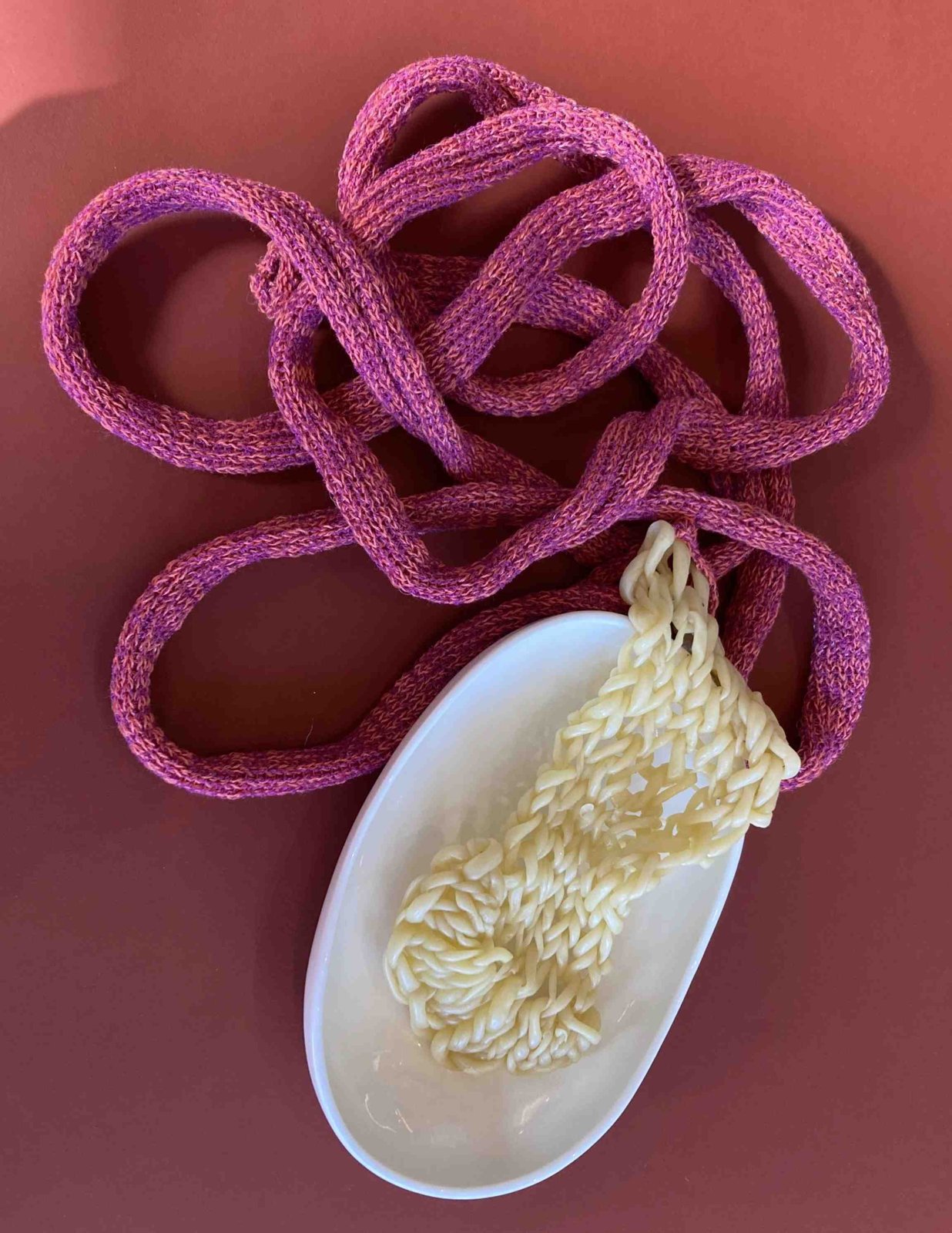 Pink knitted cord and a pale yellow knitted piece on a white dish