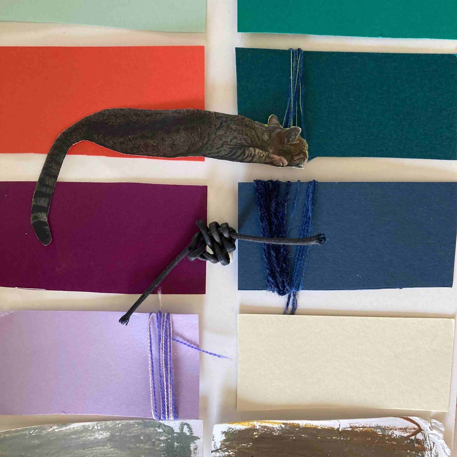Cat-shaped textile resting on coloured paper swatches with threads